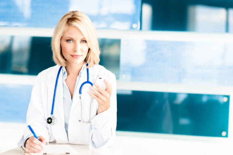 Blond Woman Doctor in Office with Mobile Phone