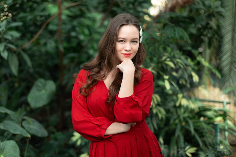 Beautiful elegant young girl in red dress makes a symbol of love. Teen girl showing a heart sign on the camera, expresses romantic feelings, expresses sincere positive feelings. I love you concept