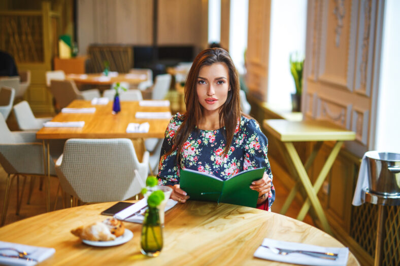 beautiful woman making the order in restaurant. Girl holds in the hands of the menu. She is dressed in a beautiful blue dress