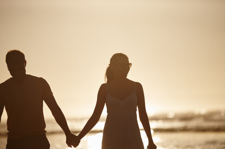 Walking, love or couple holding hands at beach for valentines day, sunset or romance. Summer vacation, silhouette or people bonding on holiday at sea in Spain for romantic honeymoon or travel date.