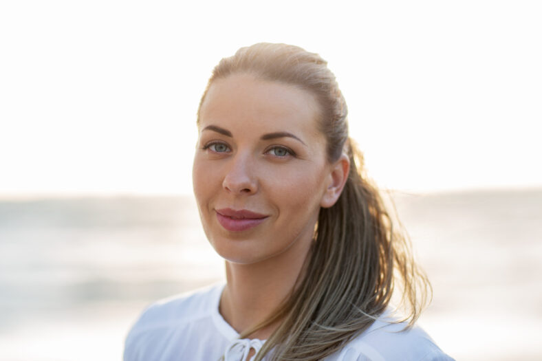 people, facial expression and emotion concept - happy young woman face on beach