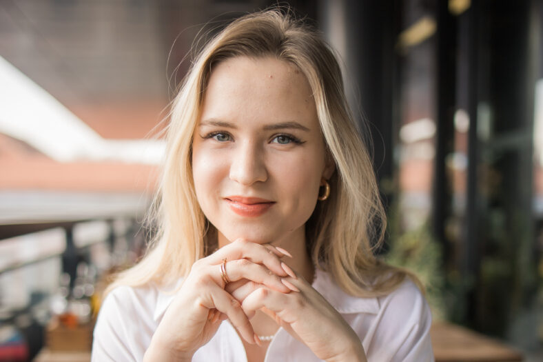 Portrait of beautiful young blonde woman drinking a cup of tea in balcony cafeteria. Happy smiling female relaxing in a coffee shop