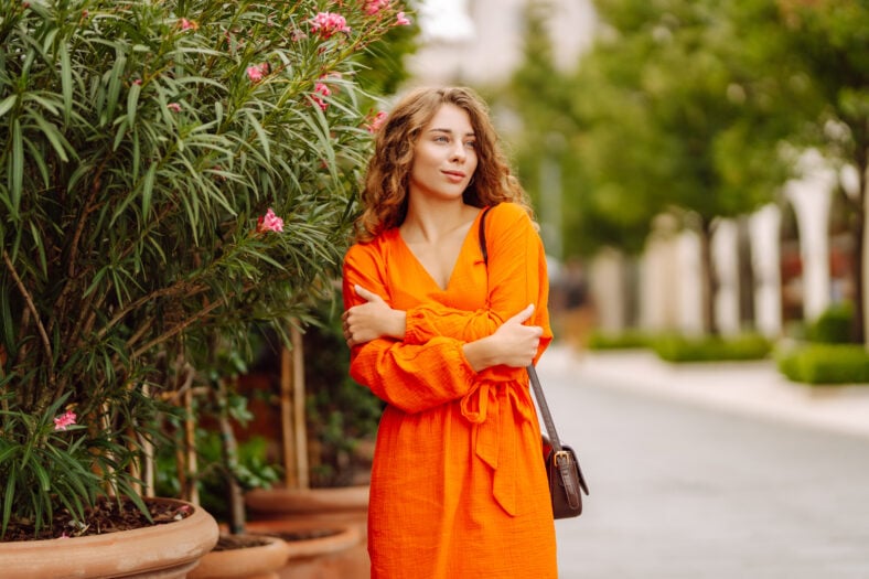 Cheerful tourist in a bright dress walks along a beautiful street. A young woman enjoys the weather outdoors. The concept of walking, vacation, travel. Active lifestyle.