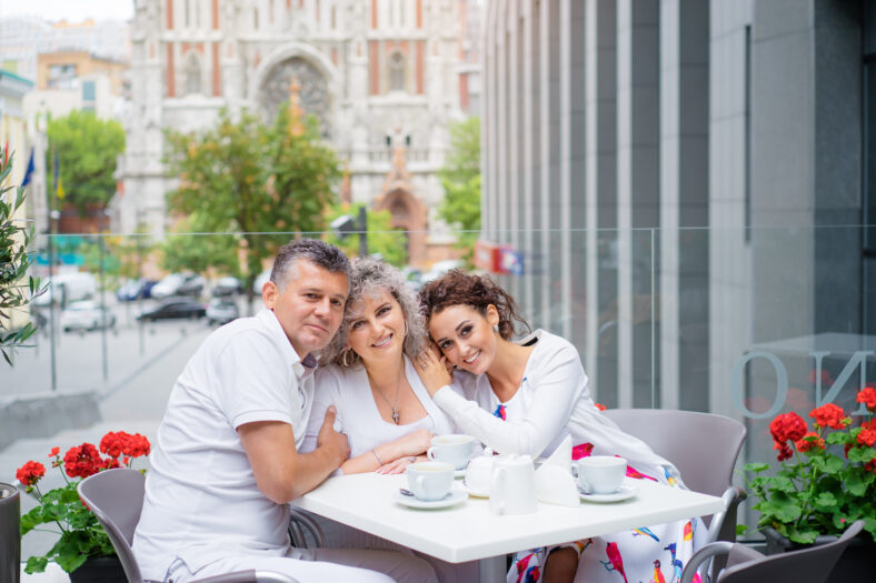 Family day. Elderly loving couple and their adult daughter smiling at camera while sitting in sidewalk cafe.