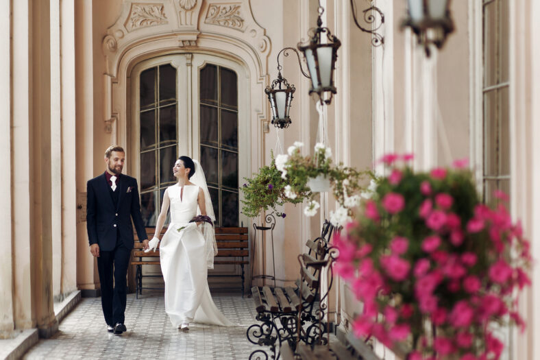 elegant gorgeous bride and stylish groom walking holding hands, sensual touch on background of old building. unusual luxury wedding couple in retro style.