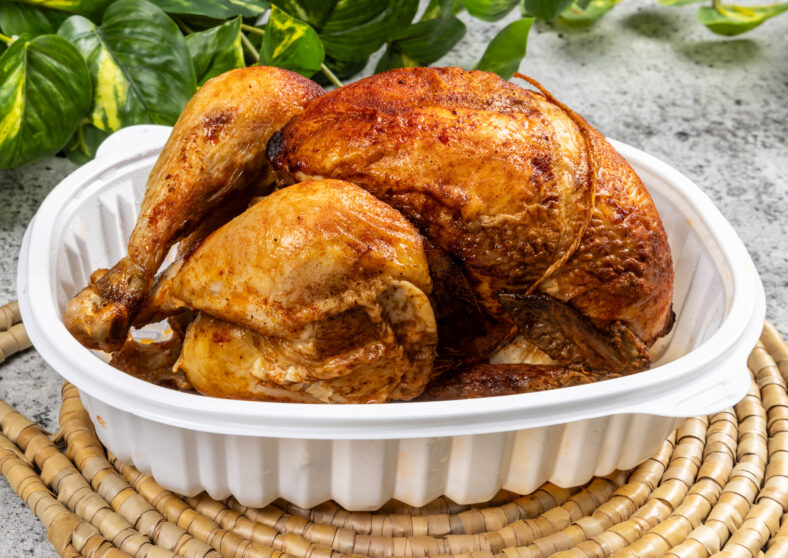 A whole rotisserie chicken in a take out pan
