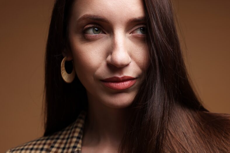 Beautiful woman in stylish outfit on brown background, closeup