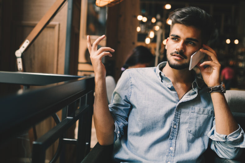 Portrait of young handsome man in blue shirt talking on phone