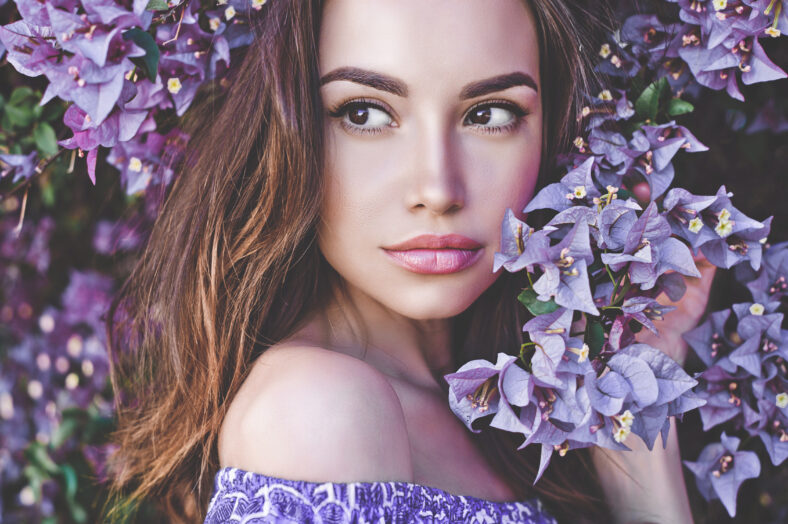 Outdoor fashion photo of beautiful young woman surrounded by flowers. Spring blossom