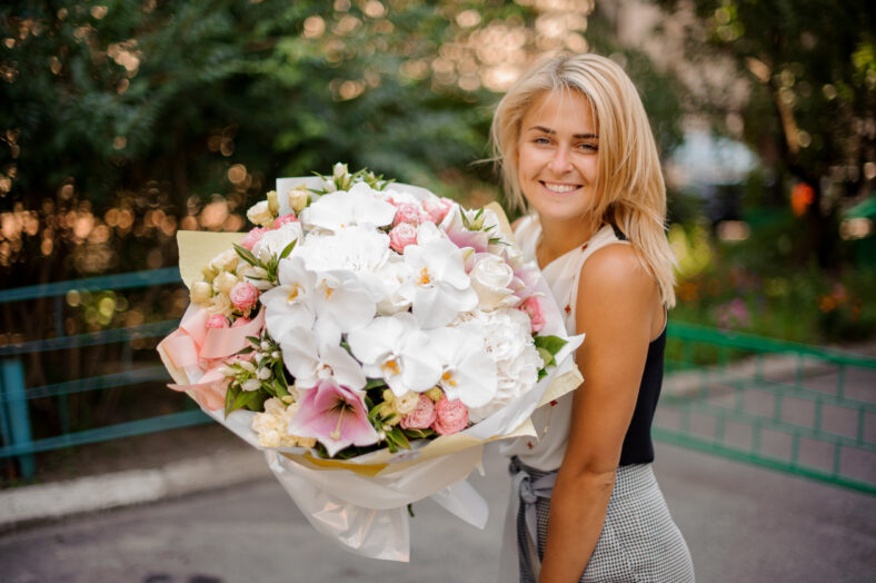 Beautiful blond girl holding a pretty and soft composition of many beautiful and colorful flowers