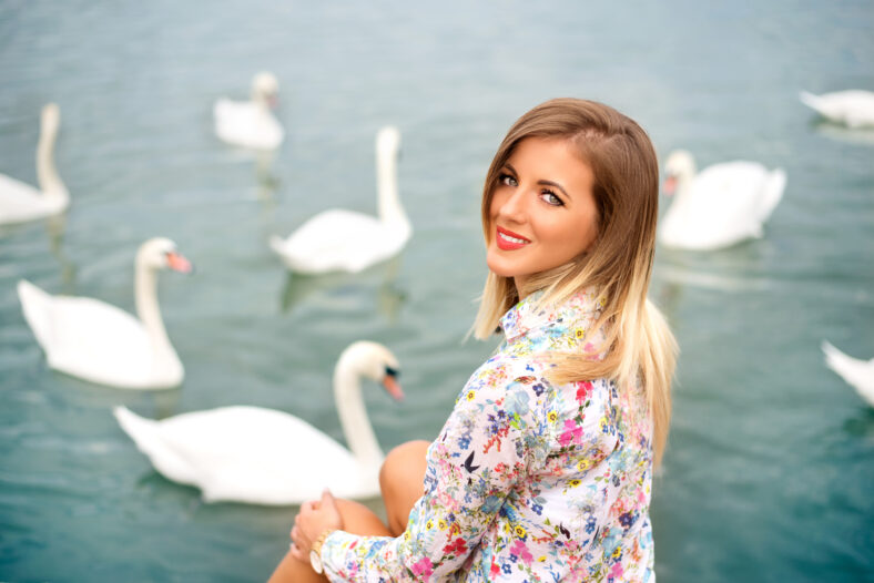 Beautiful blonde woman sitting on the beach with swans