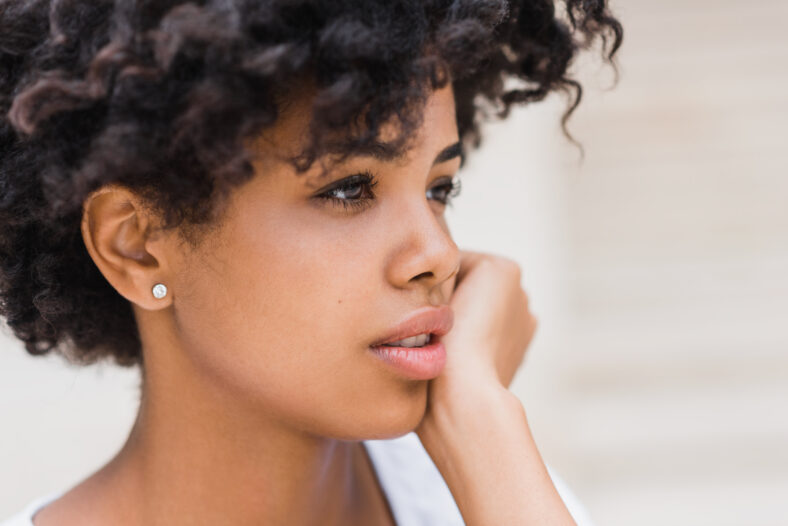 Cropped close-up shot of beautiful young dark skinned woman wearing casual with sad, pensive, reflective look, against white wall background with copy space for your text or advertising content.