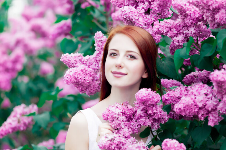 Young redhead girl in white dress in springtime garden of lilac.