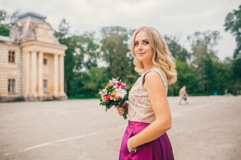 Portrait of a beautiful bridesmaid posing with bride's wedding bouquet near old castle. Amaizing wedding day.