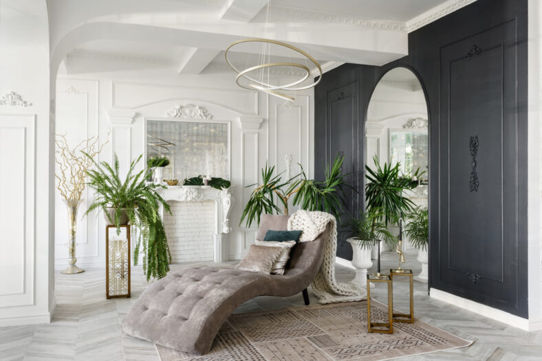 Morning in luxurious light interior in the Baroque style. Bright and clean interior design of a luxury living room with parquet wood floors, fireplace, sofa and flowers. Stucco on walls.