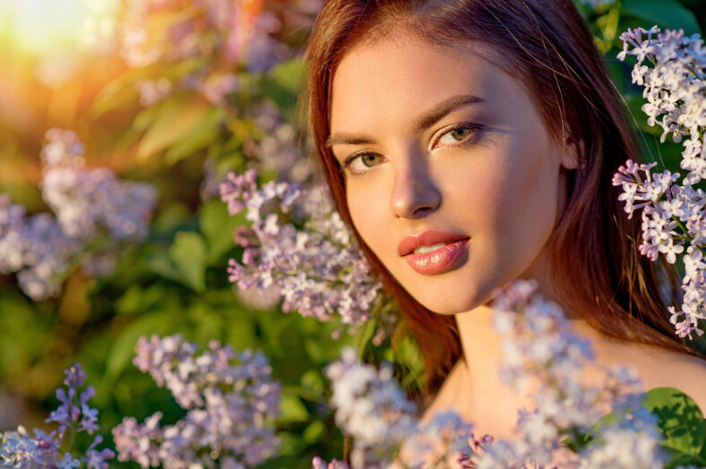 Pretty young woman posing outdoors in nature around her bush of blossoming flowers. Girl outside on a sunny summer day with white flowers. Natural flowers. Closeup face.