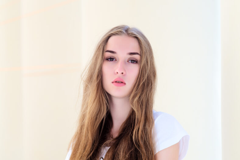 Close portrait of a beautiful teenage girl. dressed in a white T-shirt on a yellow background.