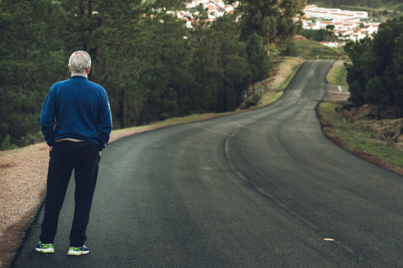 Active senior man standing on lonely road between mountains. Older man of back standing on lonely highway