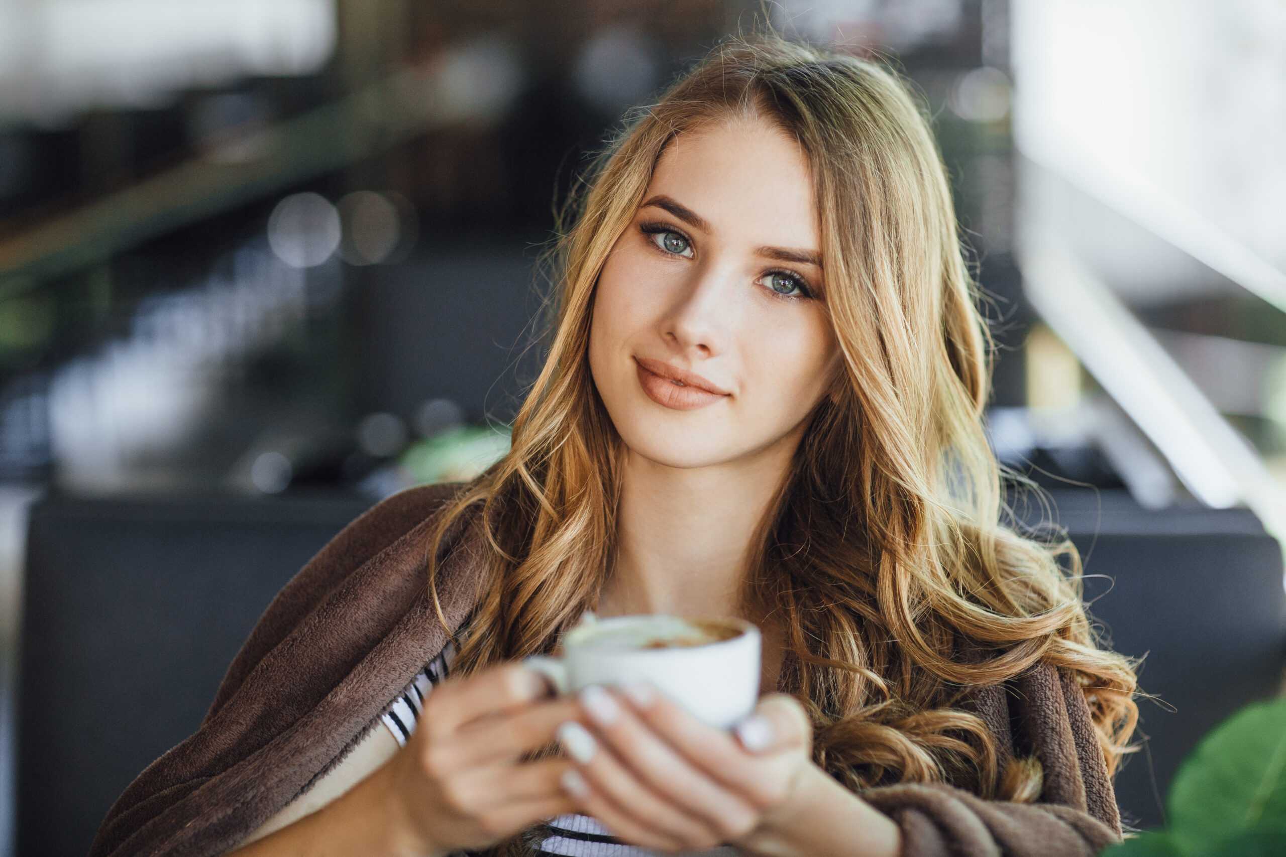 Young pretty girl blonde in casual clothes resting and drinking coffee on a summer terrace cafe. She was presented with a bunch of roses.
