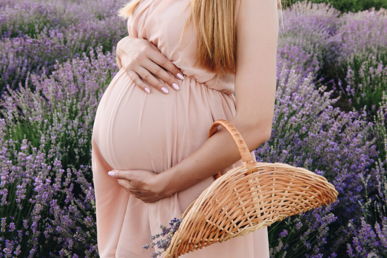 Pregnant girl blonde in a beige dress and straw hat. Lavender field. In anticipation of a child. The idea of a photo shoot. Walk at sunset. Future mom. Basket of flowers.