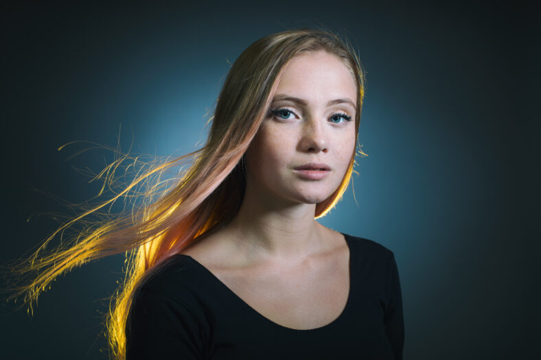 Portrait of a young woman with freckles on her face and light hair developing in the wind.