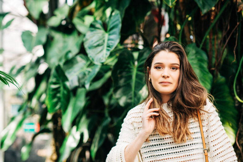 Outdoor portrait of beautiful young woman wearing white pullover, green tropical leaves on background