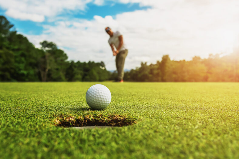 golf player putting golf ball into hole with sunshine