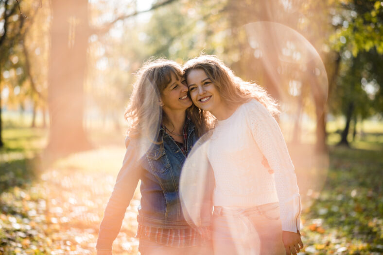Mother having great time with her adult daughter outdoor in park - flare visible
