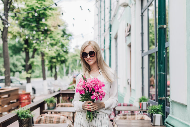 Stylish young woman with a bouquet of flowers in a summer cafe