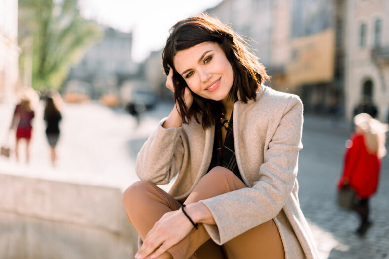 Foto de una hermosa mujer morena elegante en la ciudad vieja, con abrigo beige, pantalones marrones. Fashion Summer Photo, Close Up, Copy Space.