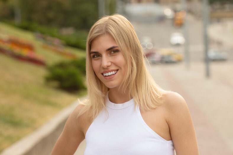 Outdoors lifestyle fashion portrait of happy stunning blonde girl. Beautiful smile. Walking to the city street. Long light hair. Joyful and cheerful woman. Happiness.