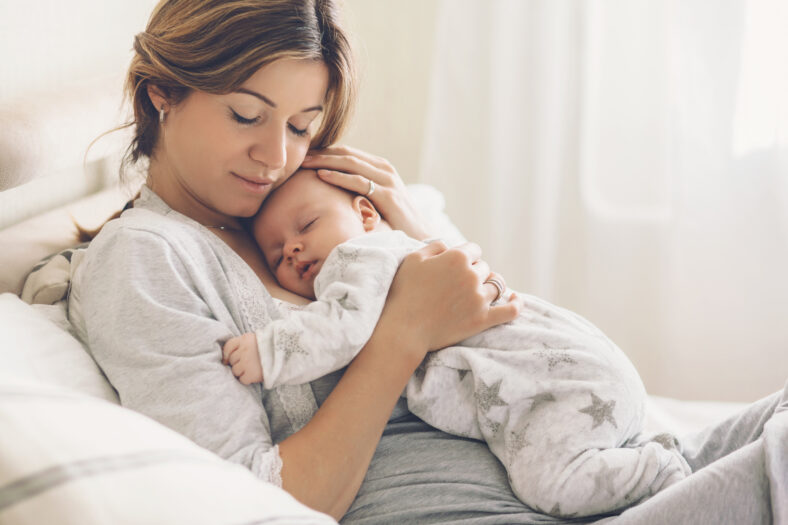 Amar a mamá cariñando de su bebé recién nacido en casa. Retrato brillante de feliz madre sosteniendo un niño infantil dormido en las manos. Madre abrazando a su pequeño hijo de 2 meses.