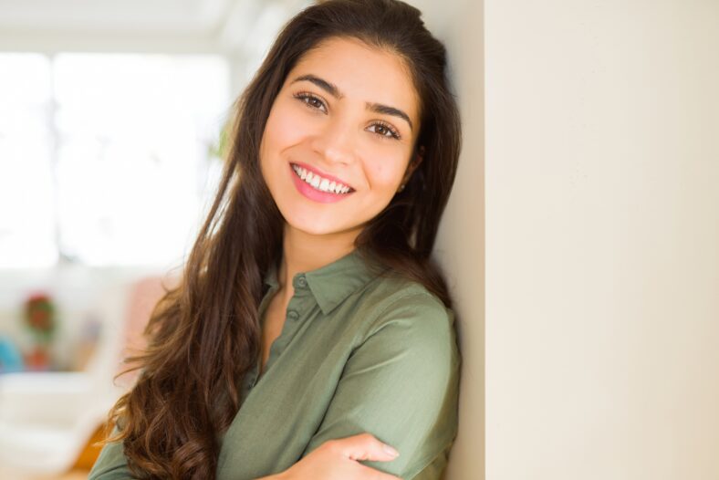 Beautiful brunette woman smiling cheerful, looking happy and positive with crossed arms
