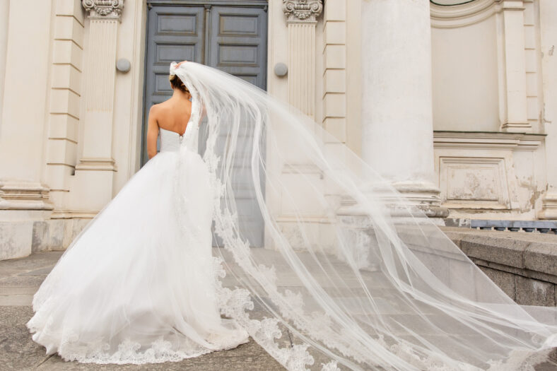 Wedding day. Bride in white wedding dress holding long veil with embroidery