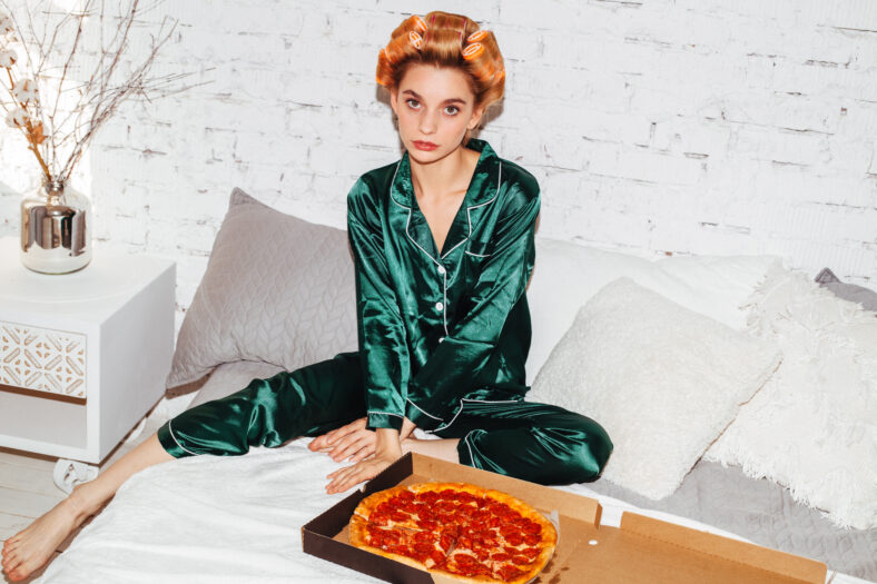 nice woman in pajamas doubting with pizza box in bed
