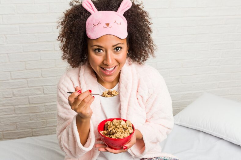Young african american woman eating a cereal bowl on the bed