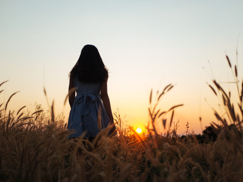 Trendy girl in stylish summer dress feeling free in the field with flowers in sunshine.