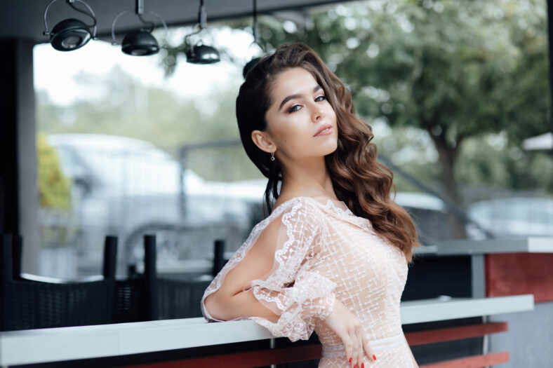 Beauty fashion portrait. Sexy face of an attractive lady posing in dress. Photo girl with perfect skin ourdoor. Beautiful woman with long brown curly hair. Fashion gorgeous woman.