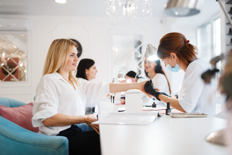 Group of girlfriends relax on manicure procedure in beauty salon. Professional beautician and female customers, nail care in spa, fingernail treatment