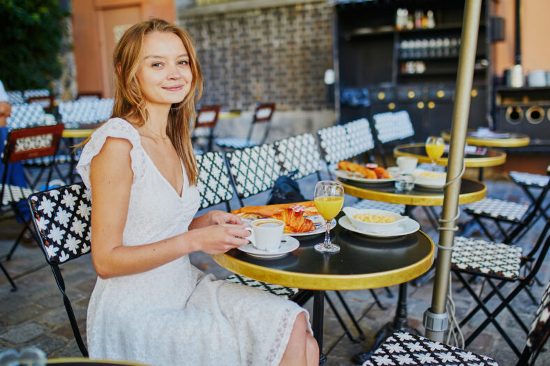 Cheerful young woman having breakfast or brunch in traditional French cafe on Montmartre in Paris, France