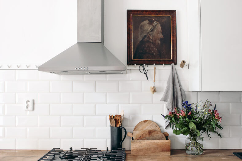 Interior de cocina ecléctica moderna. Muro de ladrillo blanco con baldosas de metro, rieles de clavija y pintura al óleo. Encimera de madera, campana de acero inoxidable y estufa de gas. Diseño escandinavo, puesta en escena, concepto.