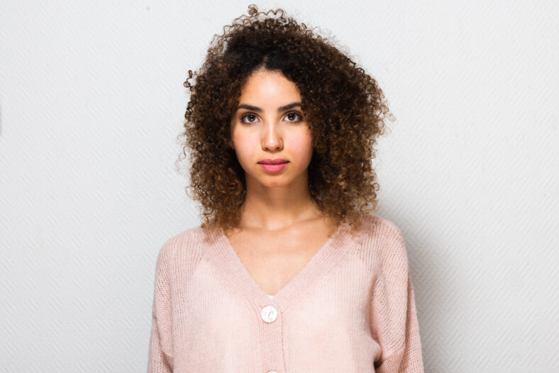 Retrato delantero por la parte delantera de una joven seria afroamericana con cabello rizado por fondo blanco