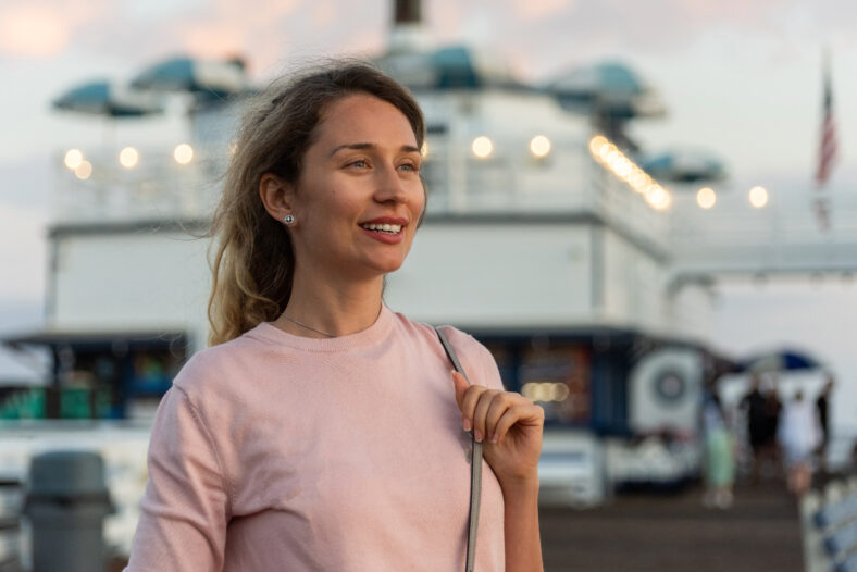 Feliz mujer rubia en suéter rosa en el muelle de Malibu, California