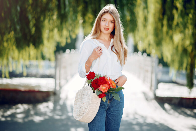 Beautiful girl in a white blouse. Woman in a summer city. Lady with bouquet of flowers