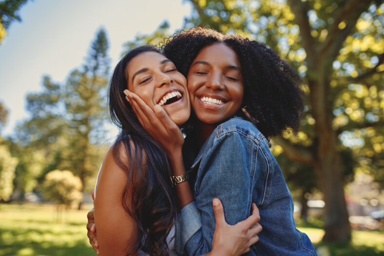 Diverse smiling female friends hugging each other in the park laughing and having fun