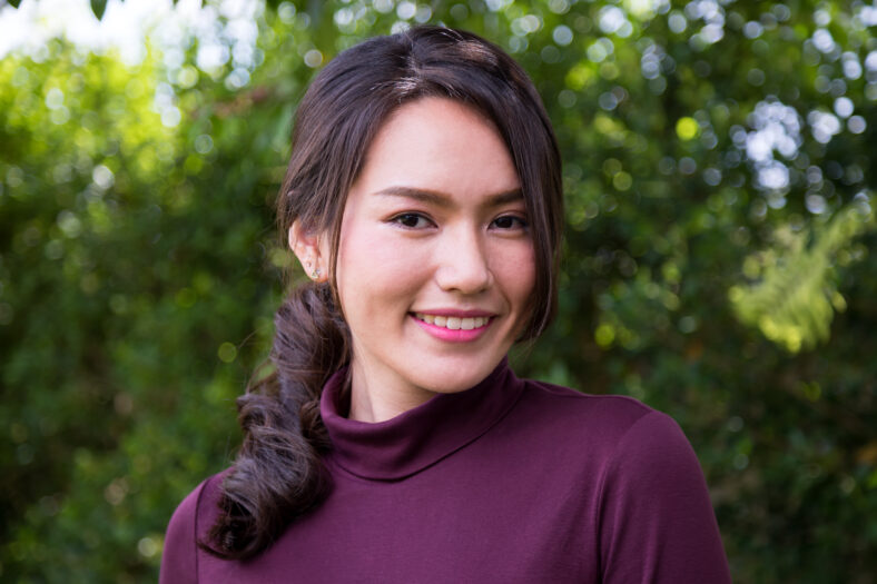 Portrait of a young Asian woman smiling while standing in park with bokeh; Woman's face with make-up and hairstyle