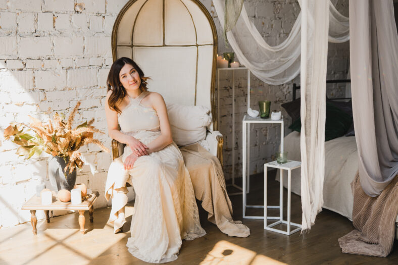 Beautiful young caucasian woman in white lace dress posing for photo in decorated vintage room. Long dark hair. Woman portrait indoors. Beauty, health care concept.