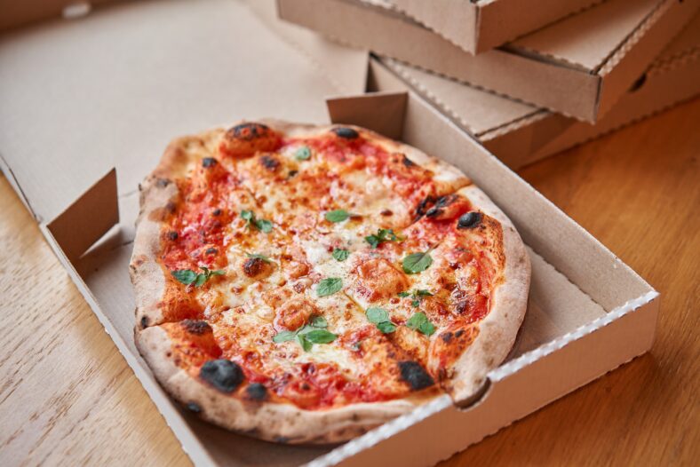Pizza delivery concept. Baked products in a cardboard box against a wooden background. Baked tasty margherita pizza in Traditional wood oven in Neapolitan restaurant, Italy
