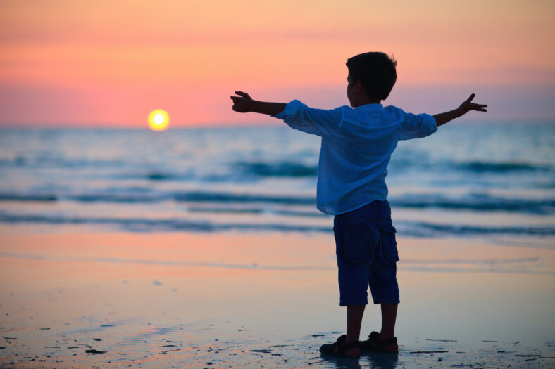 Little boy silhouette on beach at sunset