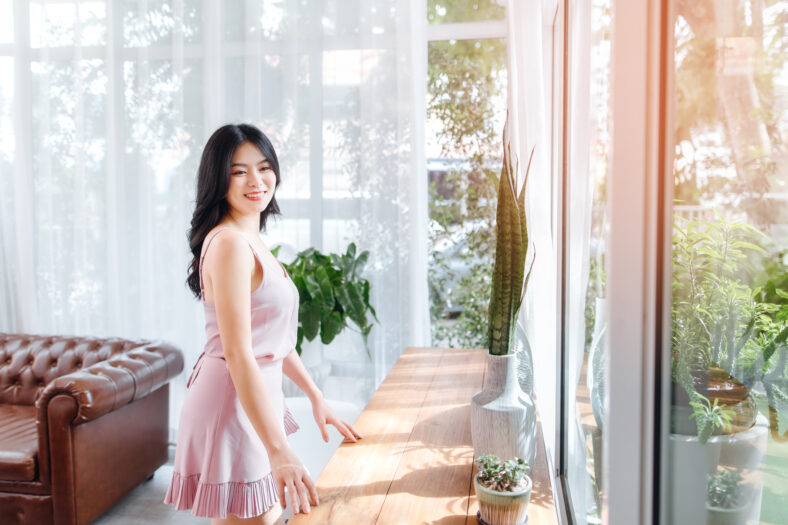 Beautiful Asian woman wear dress pants pink. Leaning against a wooden table in coffee shop.